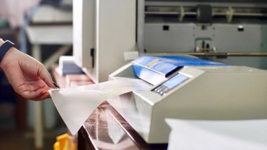 Kadın tipografide laminasyon makinesi laminatöründe kağıt lamine ediyor.