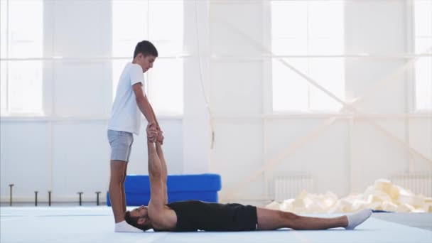 一个合适的男人和一个十几岁的孩子正在健身房练习杂技手架. — 图库视频影像
