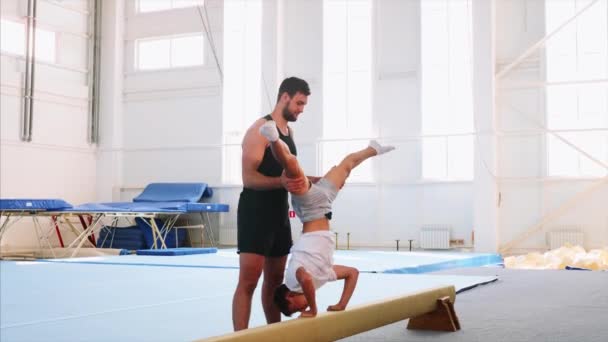 Een jonge atleet is het maken van een handstand op Beam en push-up Headfirst, zijaanzicht. — Stockvideo