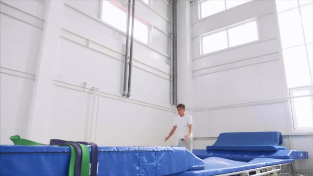 Chłopiec sportowiec robi z powrotem Flip na trampoliny w siłowni, powolny ruch. Widok z boku. — Wideo stockowe