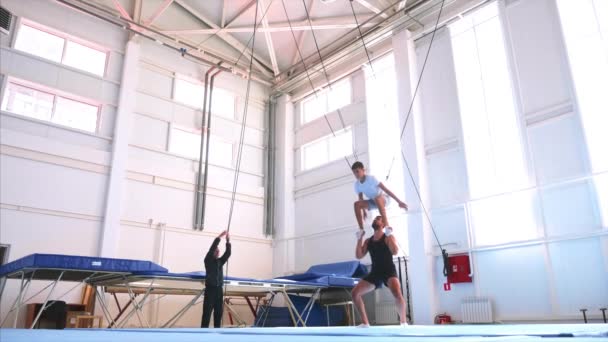 Um jovem atleta está fazendo um flip back ar nas fundas de segurança no ginásio . — Vídeo de Stock