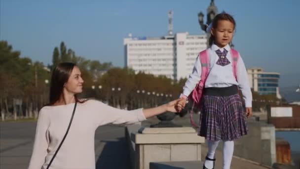 Escola menina está andando sobre trilhos de beira-mar com a mãe, steadicam, vista frontal . — Vídeo de Stock