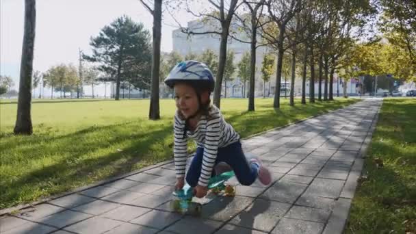 En flicka som sitter på en skateboard och trycka sig själv med ett ben, Steadicam. — Stockvideo