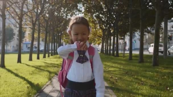Ένα μικρό κορίτσι με σχολική στολή περπατάει και μιλάει με έξυπνα ρολόγια. — Αρχείο Βίντεο