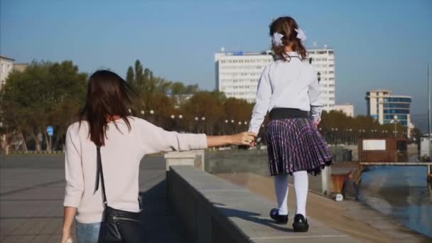 Escola menina está andando sobre trilhos de beira-mar com a mãe, steadicam, visão traseira . — Vídeo de Stock