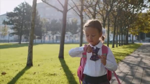 Seorang gadis kecil berseragam sekolah sedang berjalan dan berbicara dengan jam tangan pintar . — Stok Video
