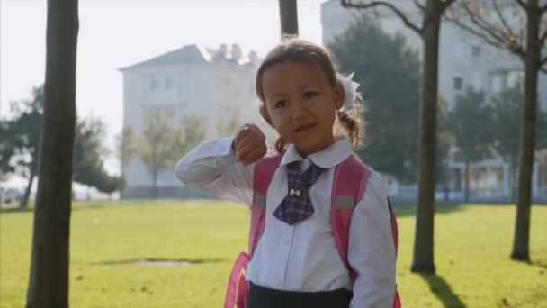 Seorang gadis kecil berseragam sekolah berdiri dan berbicara dengan jam tangan pintar . — Stok Video