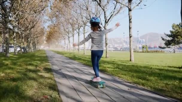 Little girl is slowly skateboarding in protective helmet, steadicam shot. — Stock Video