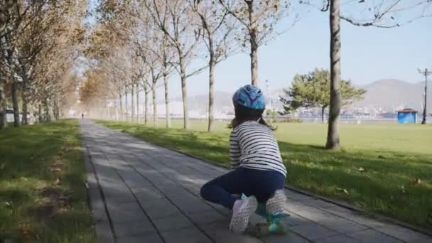 Uma menina sentada em um skate e empurrando-se com uma perna, steadicam . — Vídeo de Stock