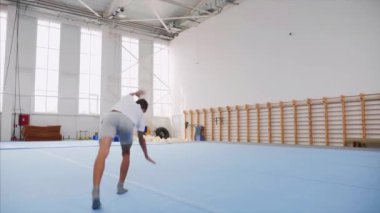 Bir genç çocuk spor salonunda bir takla ve üçlü geri flip yapıyor, steadicam.