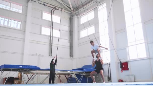 Genç bir atlet spor salonunda güvenlik sapanlar üzerinde bir hava geri flip yapıyor. — Stok video