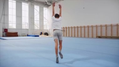 Bir genç çocuk spor salonunda bir takla ve üçlü geri flip yapıyor, steadicam.