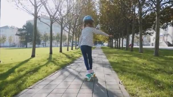 Little girl is slowly skateboarding in protective helmet, steadicam shot. — Stock Video