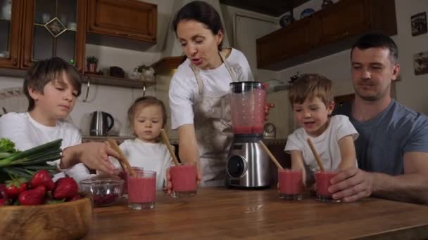 両親との子供たちは、家庭のキッチンでスムージーを準備し、それを飲む — ストック動画