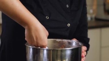 Aşçı, tatlı yapmak için çelik kâseye kahverengi krema karıştırıyor.