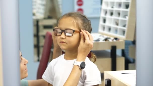 Madre con hija pequeña está eligiendo gafas en la tienda de óptica — Vídeos de Stock