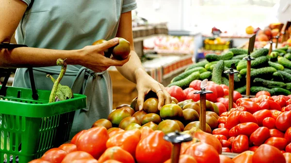 Vrouw met boodschappenmandje kiest groenten in supermarkt. — Stockfoto