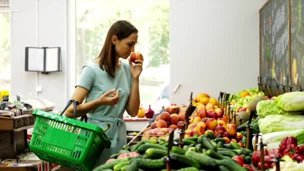 Vrouw met boodschappenmandje kiest perziken in supermarkt. — Stockvideo