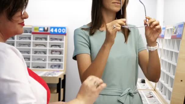 Opticien helpt de klant bij het kiezen van een bril in een optische winkel. — Stockvideo