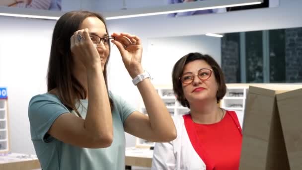 Optisi membantu klien untuk memilih kacamata di toko optik. — Stok Video