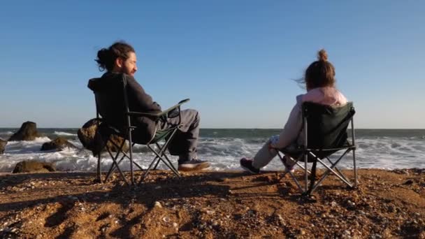 Pai com filhinha senta-se em cadeiras na praia, vista traseira. — Vídeo de Stock