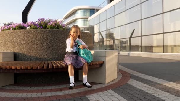 Kleine leerling in schooluniform eet appel op de bank. — Stockvideo