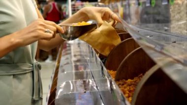 Genç beyaz kadın markette kuru üzüm yiyor.