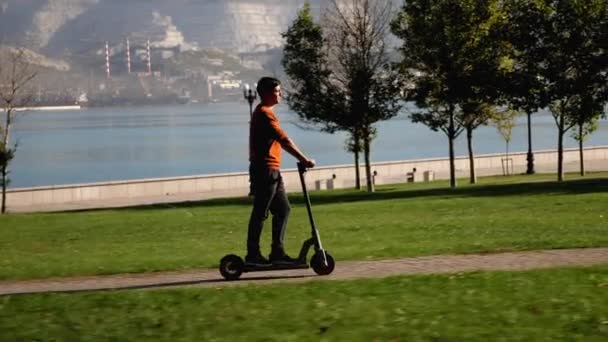 Un hombre está montando scooter eléctrico en la zona del parque de la ciudad en la mañana soleada — Vídeo de stock