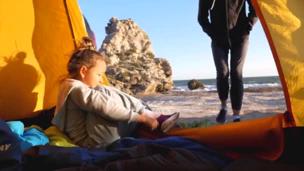 Mamá ayuda a su hija pone sus zapatos mientras ella se sienta en la tienda de campaña en la playa — Vídeos de Stock