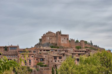 Huesca ilindeki bir ortaçağ İspanyol köyü olan Alquezar 'ın panoramik manzarası, sıcak tonlu taş evleri ve kayalık yamaçlar boyunca uzanan kil çatıları. Kompozisyon, tepenin üstündeki eski şatoyu ve kolej kilisesini ele geçiriyor.