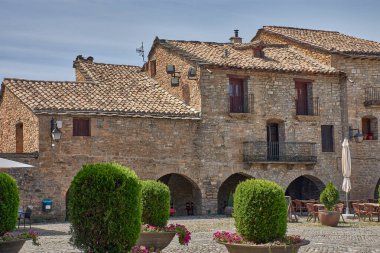 Ainsa Plaza Belediye Başkanı ortaçağ karakterini taştan evler, balkonlar ve ziyaretçileri ağırlayan teraslarla koruyor. Turistler, tarihi ve kültürel turizmi yansıtan temiz bir gökyüzünün altındaki kaldırımlı alanda geziniyorlar.