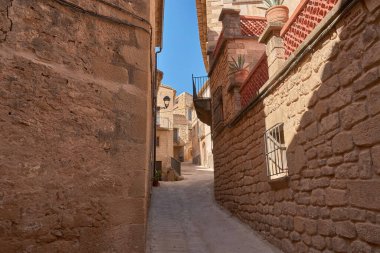 Dar sokakların özü ve Calaceite köyünün taş mimarisi. Görüntüler, mavi gökyüzünün altındaki kaldırım taşlarından, tarihi kemer ve merdivenlerin detaylarına kadar uzanan farklı perspektifleri gösteriyor.. 