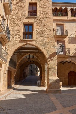 Dar sokakların özü ve Calaceite köyünün taş mimarisi. Görüntüler, mavi gökyüzünün altındaki kaldırım taşlarından, tarihi kemer ve merdivenlerin detaylarına kadar uzanan farklı perspektifleri gösteriyor.. 