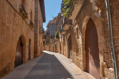 Dar sokakların özü ve Calaceite köyünün taş mimarisi. Görüntüler, mavi gökyüzünün altındaki kaldırım taşlarından, tarihi kemer ve merdivenlerin detaylarına kadar uzanan farklı perspektifleri gösteriyor.. 