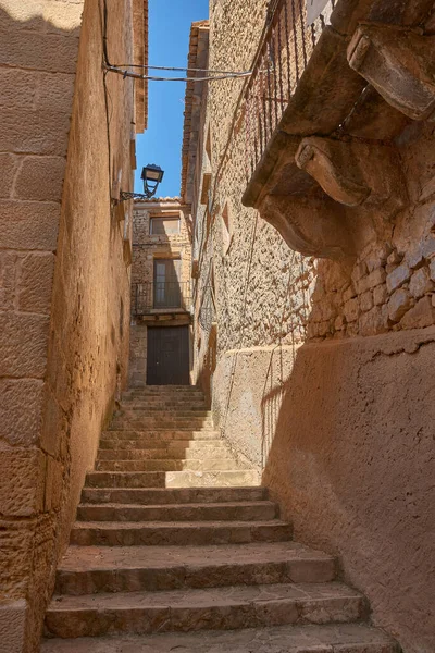 Dar sokakların özü ve Calaceite köyünün taş mimarisi. Görüntüler, mavi gökyüzünün altındaki kaldırım taşlarından, tarihi kemer ve merdivenlerin detaylarına kadar uzanan farklı perspektifleri gösteriyor.. 