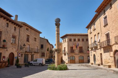 Kretas, Aragon, İspanya-4 Eylül 2025. Kretas, Teruel 'in büyüleyici köyünün Plaza Belediye Başkanı, parlak mavi gökyüzünün altında. Çakıl taşı meydanının ortasında, orijinal bir taş sütun yükselirken, çevreleyen toprak tonlu binalar...