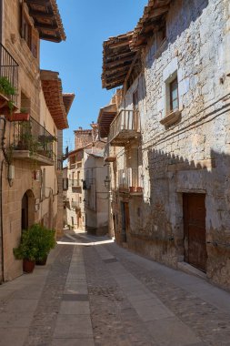 Cobblestone alley of Valderrobres, Teruel, a town that radiates history and charm. Sunlight falls on the ancient stone facades, creating a dynamic play of light and shadow that highlights the texture of the walls and uneven pavement