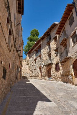 Cobblestone alley of Valderrobres, Teruel, a town that radiates history and charm. Sunlight falls on the ancient stone facades, creating a dynamic play of light and shadow that highlights the texture of the walls and uneven pavement