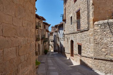 Cobblestone alley of Valderrobres, Teruel, a town that radiates history and charm. Sunlight falls on the ancient stone facades, creating a dynamic play of light and shadow that highlights the texture of the walls and uneven pavement