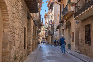 Valderrobres, Aragon, İspanya - 4 Eylül 2025, Turistler Valderrobres, Teruel 'in ortaçağ köyünün dar ve kaldırımlı sokaklarında geziniyorlar. Güneş ışığı, toprak taştan binaları aydınlatır.