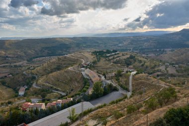 Morella 'nın duvarlı tepenin tepesinden, çevresindeki geniş bir manzara gözler önüne seriliyor, kayan tepeler, bitkilerle kaplı vadiler, dolambaçlı yollar ve kırmızımsı çatıları olan küçük ev kümeleri.. 