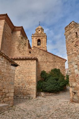 Santa Margarita 'nın görkemli kilisesi, karakteristik sıcak tonlu çan kulesi ve Barok detaylarıyla, heybetli bir şekilde taştan evlerin ve hayali ortaçağ köyü Mirambel, Teruel' in kırmızımsı çatılarının üzerine yükselir.. 