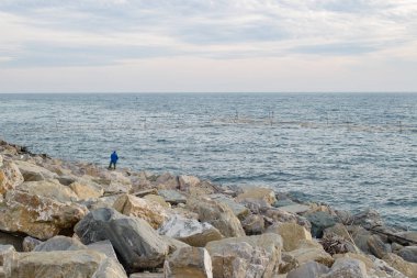 Balıkçı kayalıklarda kıyıda duruyor.
