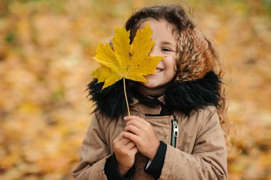 Sonbahar parkında akçaağaç yaprağı tutan tatlı küçük kız.