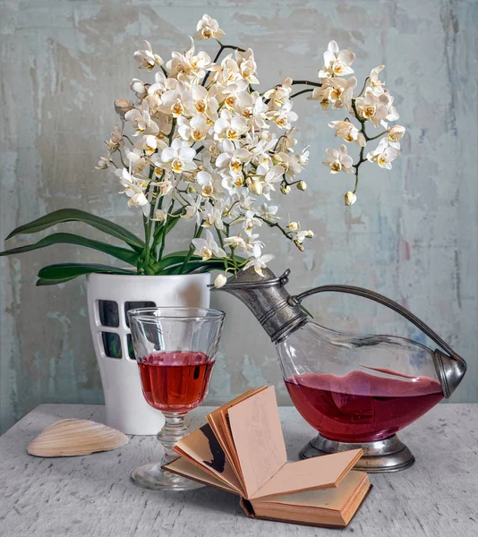 Still-life with a branch of blossoming orchids, wine and a book. Vintage. Retro.