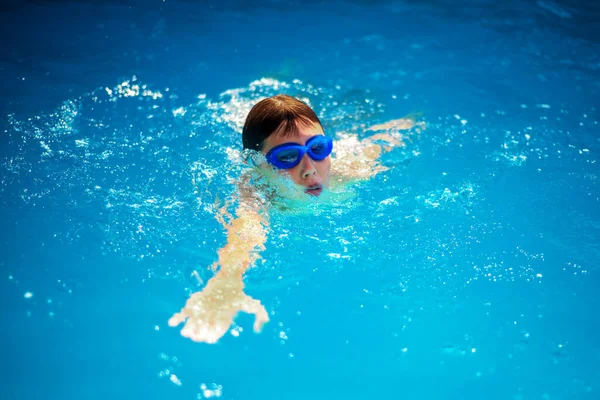Kisfiú atléta úszik a medencében a csúszda mellett. A képzés és a gyermeksportok fogalma — Stock Fotó
