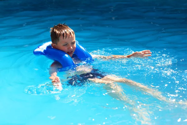 Um menino nada na piscina com um colete inflável. O conceito de esporte e estilo de vida saudável . — Fotografia de Stock