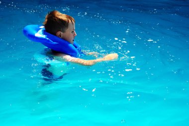 Küçük çocuk havuzda şişme yelekle yüzmeyi öğreniyor.