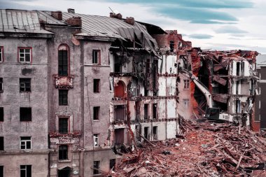 Bir kazıcı Norilsk şehrinde yıkılan eski bir tuğla evi yıkıyor apartman yıkım bloğu. Rusya 'daki eski evler. Buldozer eski binayı yıktı.