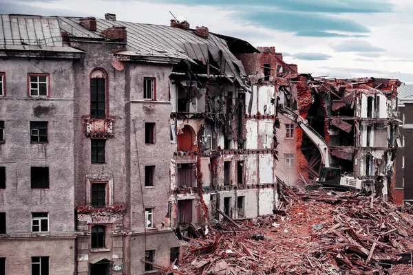 Bir kazıcı Norilsk şehrinde yıkılan eski bir tuğla evi yıkıyor apartman yıkım bloğu. Rusya 'daki eski evler. Buldozer eski binayı yıktı.